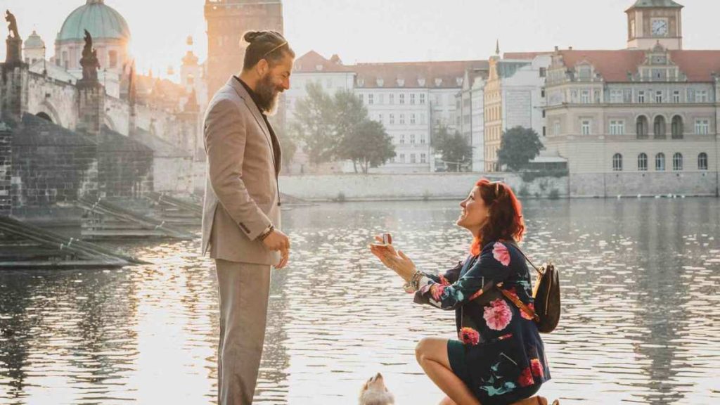 Woman proposes to a man with dog and water background with clock tower